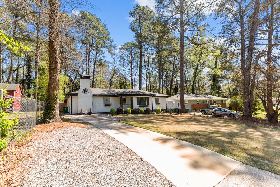 A front walkway and lawn leading to a single-story home on a tree-lined lot